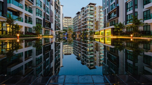 Un hotel moderno con varios pisos, grandes ventanales y una piscina reflectante en el centro.