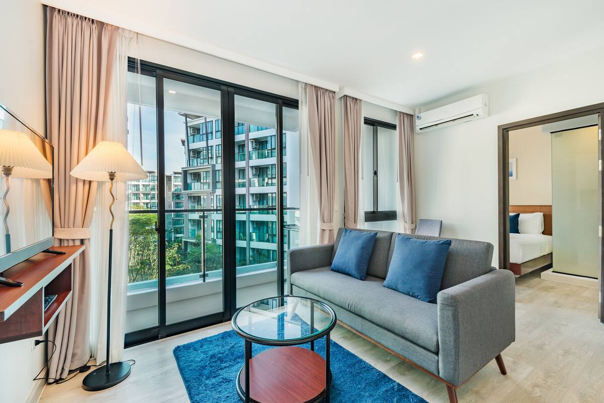 Ein modernes Wohnzimmer mit einer Couch, einem Glastisch und Blick auf ein Gebäude durch große Fenster.