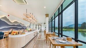 Un comedor moderno con una barra larga, sillas de madera y mesas. Amplias ventanas ofrecen vistas a un lago y montañas.