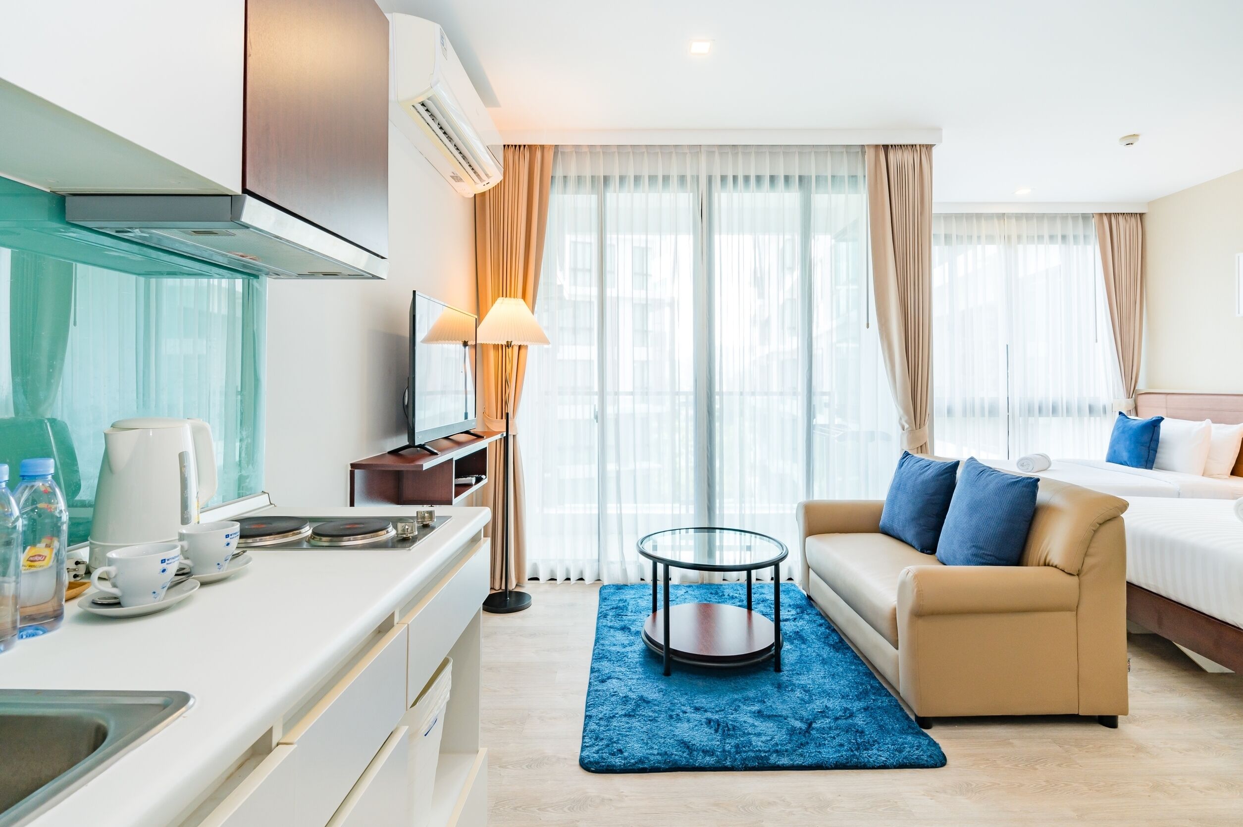 Ein Hotelzimmer mit einer Küchenzeile, einem Sofa, einem Bett, einem Fernseher und einem großen Fenster mit Vorhängen.