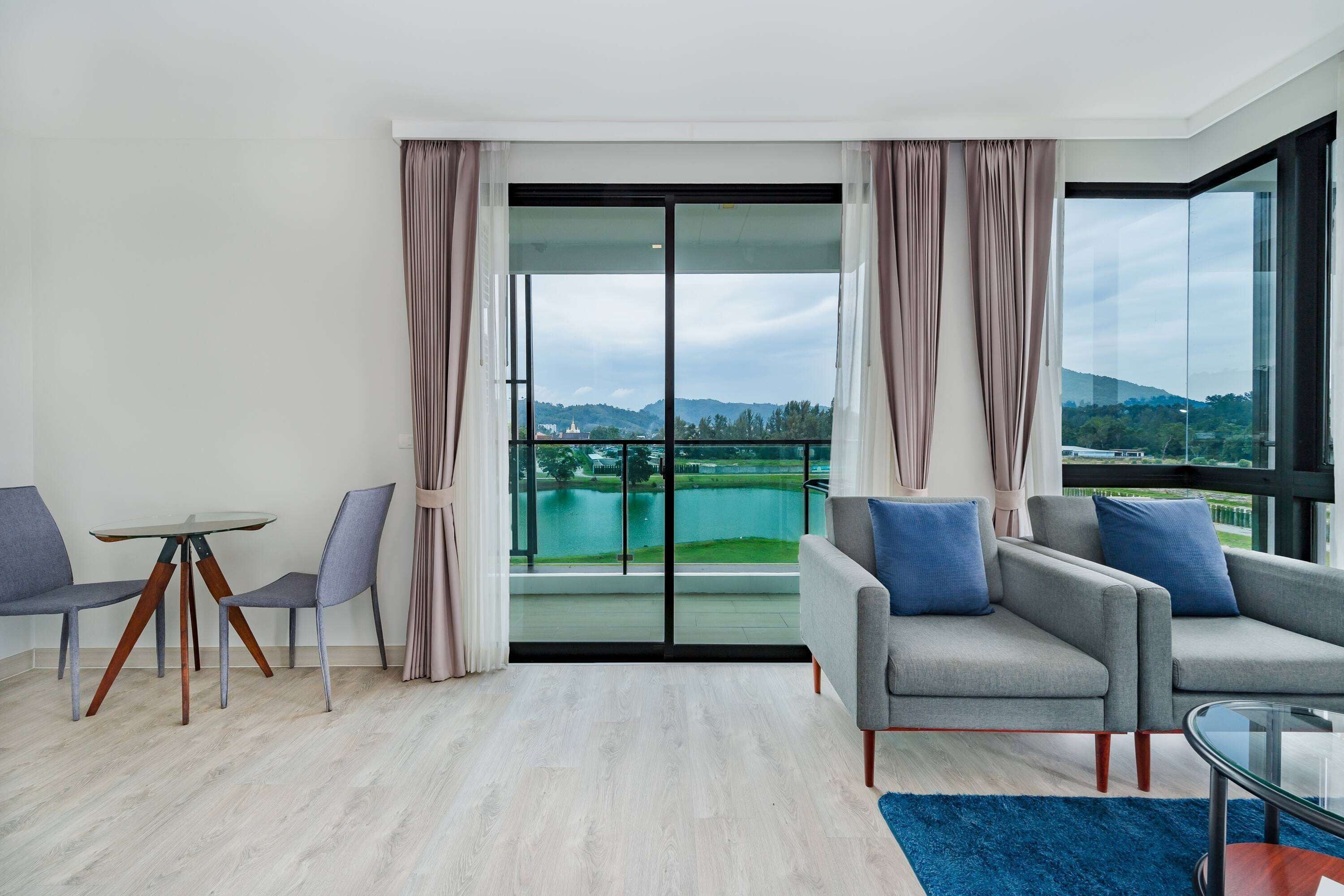 Un salon moderne doté d’une grande porte-fenêtre coulissante donnant sur un balcon avec vue sur le lac. On y trouve deux canapés gris, une petite table ronde et deux fauteuils.