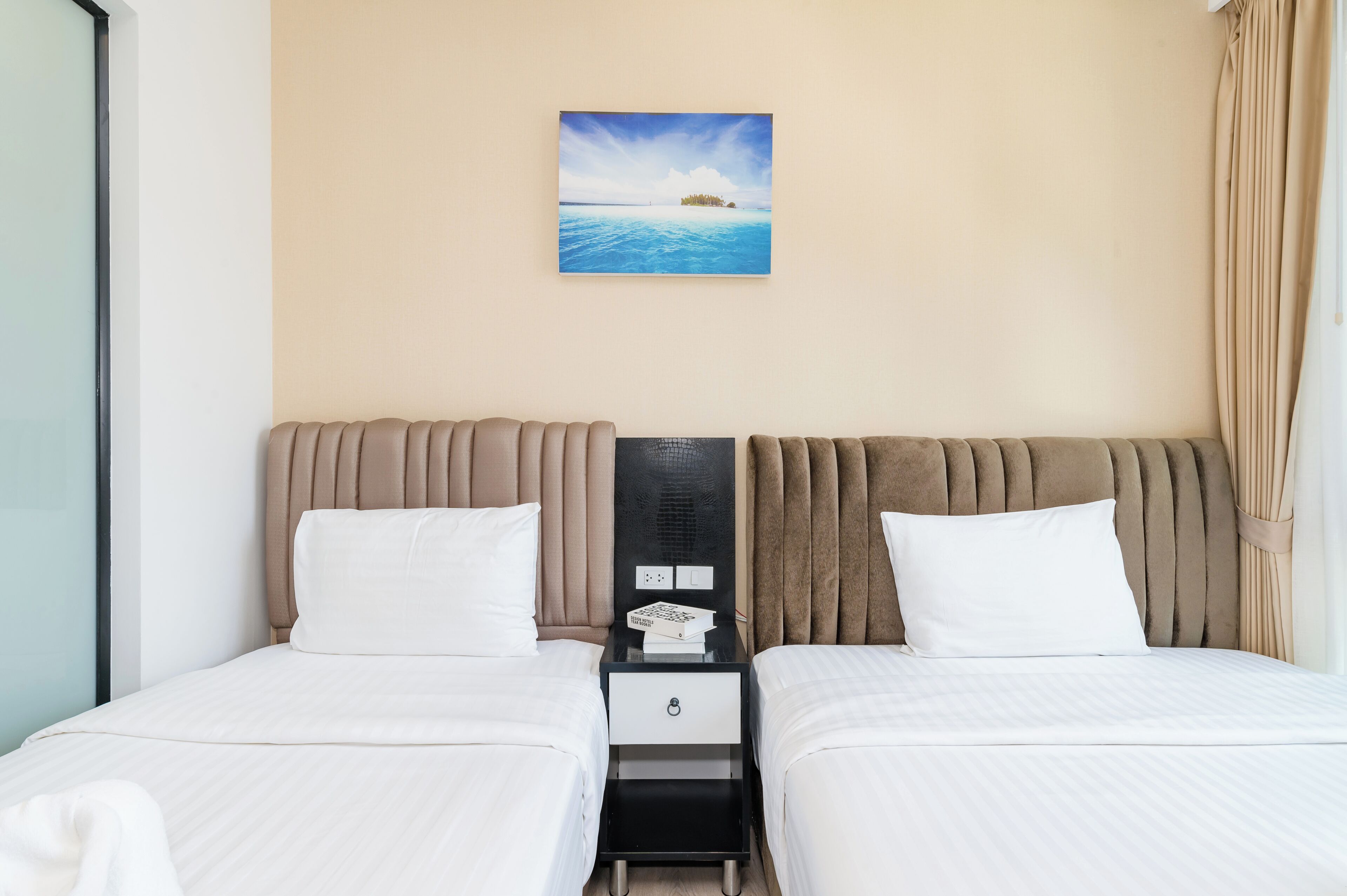 A double bed with a headboard, a small bedside table with a lamp, and a painting of a beach scene.