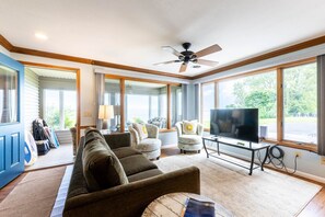 A living room with a ceiling fan, a television, and large windows.
