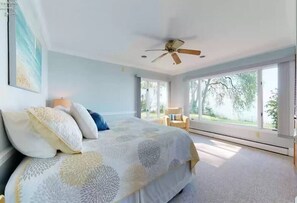 A bedroom with a large bed, a ceiling fan, and a view of the outdoors.