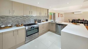 A modern kitchen with a gas stove, oven, and dishwasher, light-colored cabinets, and a tiled backsplash. - Tallowood House - A great family getaway (NULKABA)
