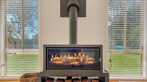 A modern fireplace with a glass front, logs beneath, and a chimney. - Tallowood House - A great family getaway (NULKABA)