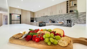 A modern kitchen with a central island, stainless steel appliances, and a stone backsplash. - Tallowood House - A great family getaway (NULKABA)