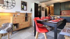 Une cuisine moderne avec des meubles en bois, une table à manger entourée de chaises rouges et une grande horloge murale.