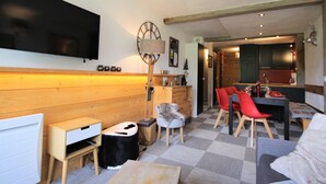 Un salon moderne avec un mur en bois, un téléviseur à écran plat, une horloge et un coin repas avec des chaises rouges.