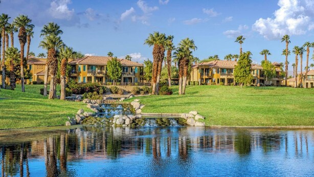 Un resort con edificios de varios pisos, una fuente central y palmeras.