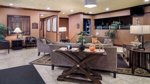 Un vestíbulo espacioso con diseño moderno, que cuenta con una zona de estar central con sofás y una mesa de centro, una recepción y un televisor montado en la pared.