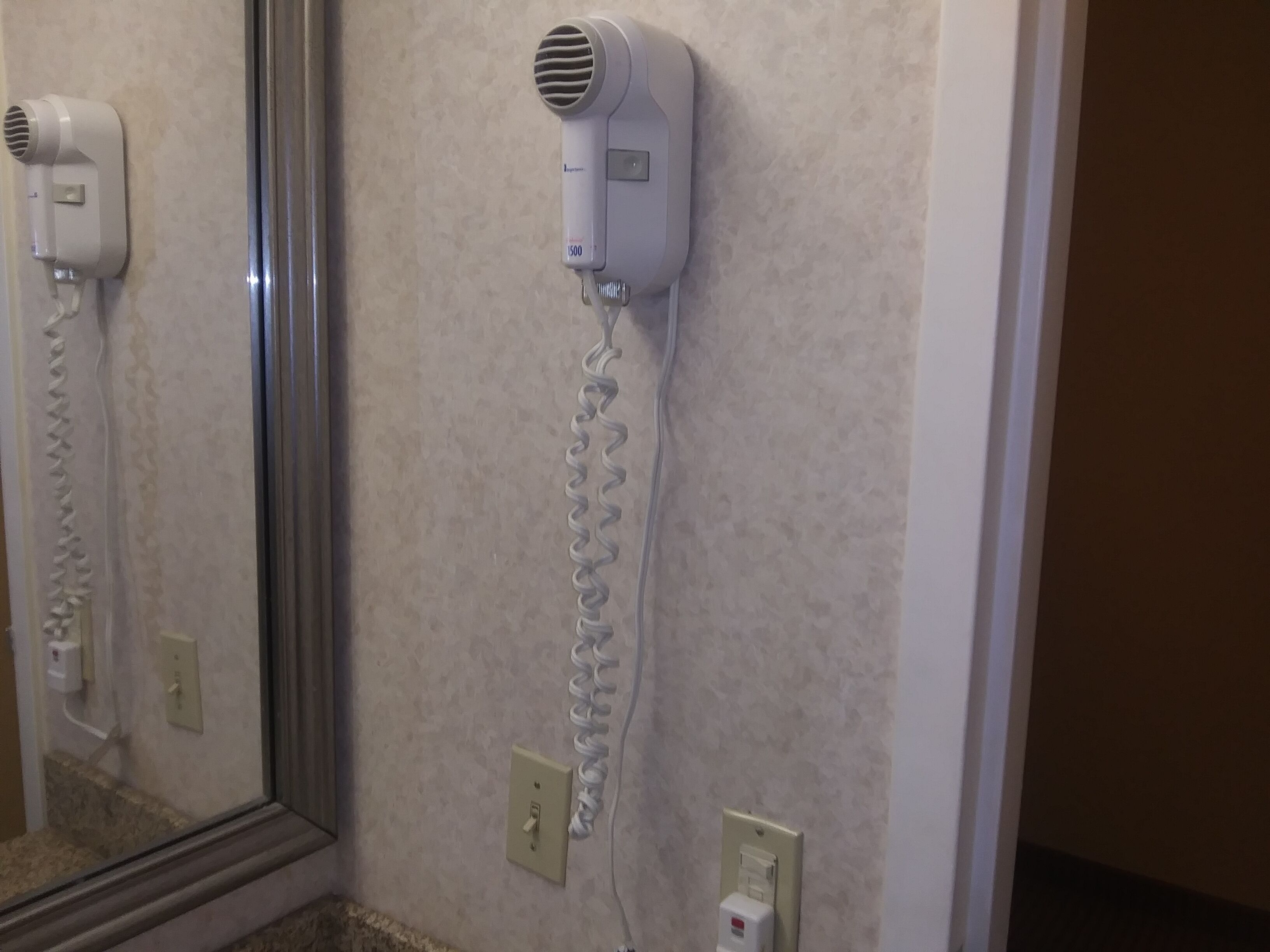 Un sèche-cheveux fixé au mur, avec un câble d’alimentation.