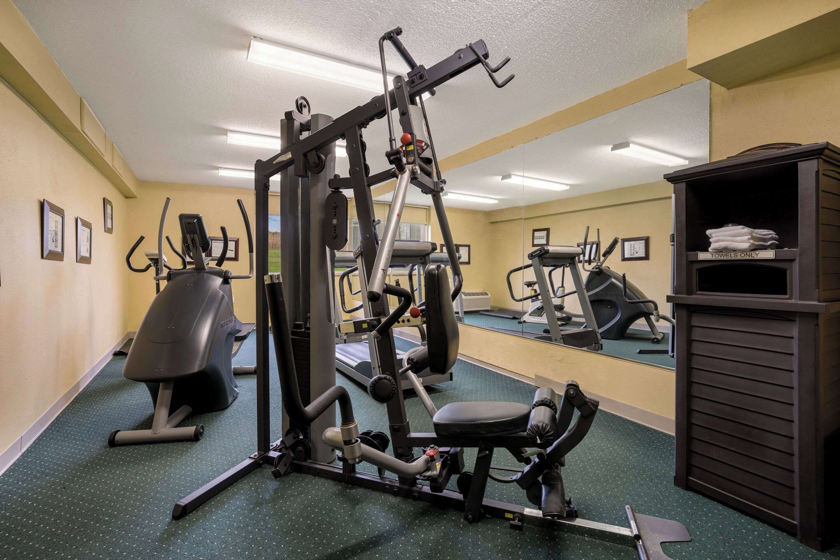 Un gimnasio con diversas máquinas de ejercicio, un espejo grande y un perchero para toallas.