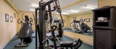 Un gimnasio con diversas máquinas de ejercicio, un espejo grande y un perchero para toallas.