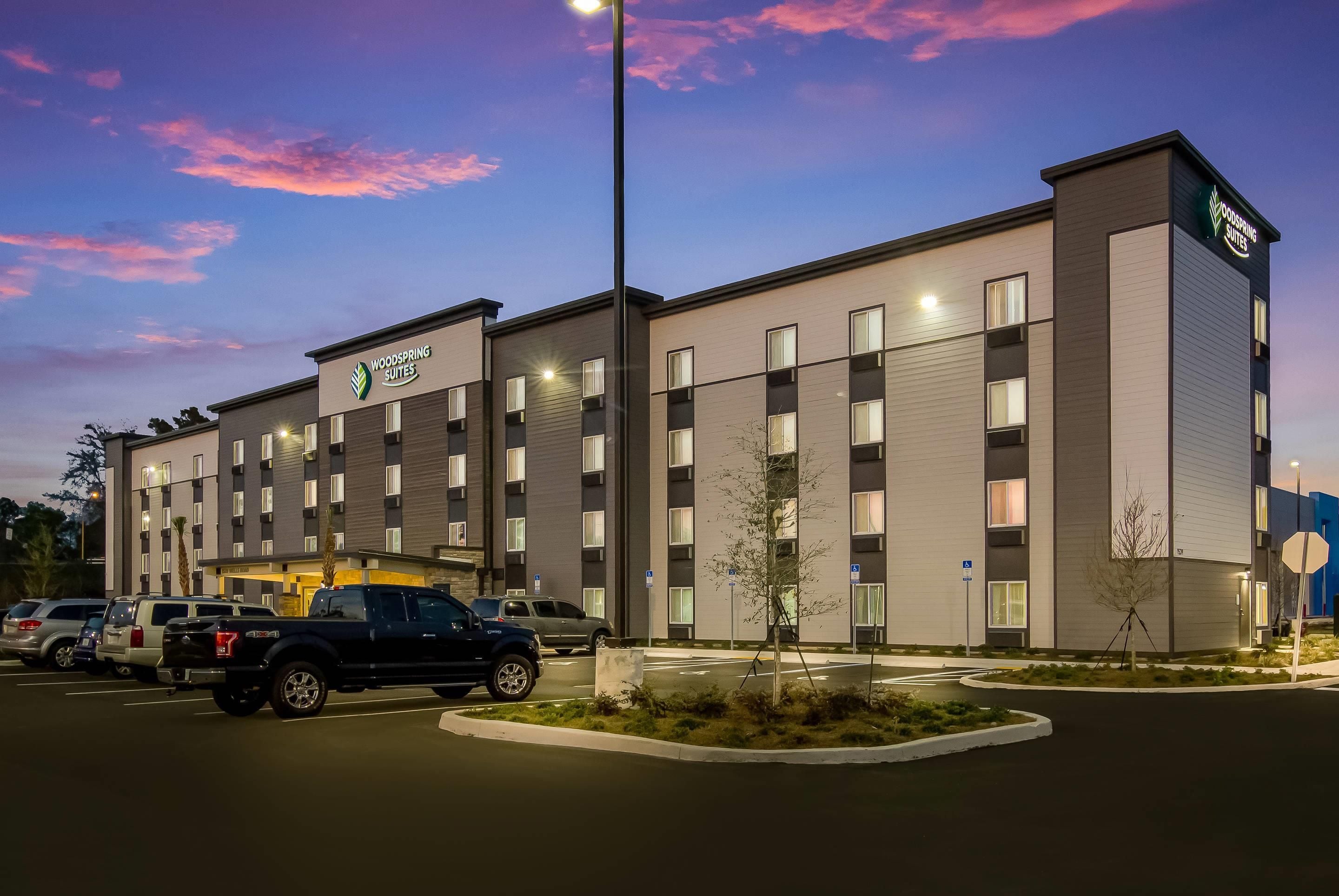 A multi-story hotel with a flat facade, a parking lot, and a clear sky.