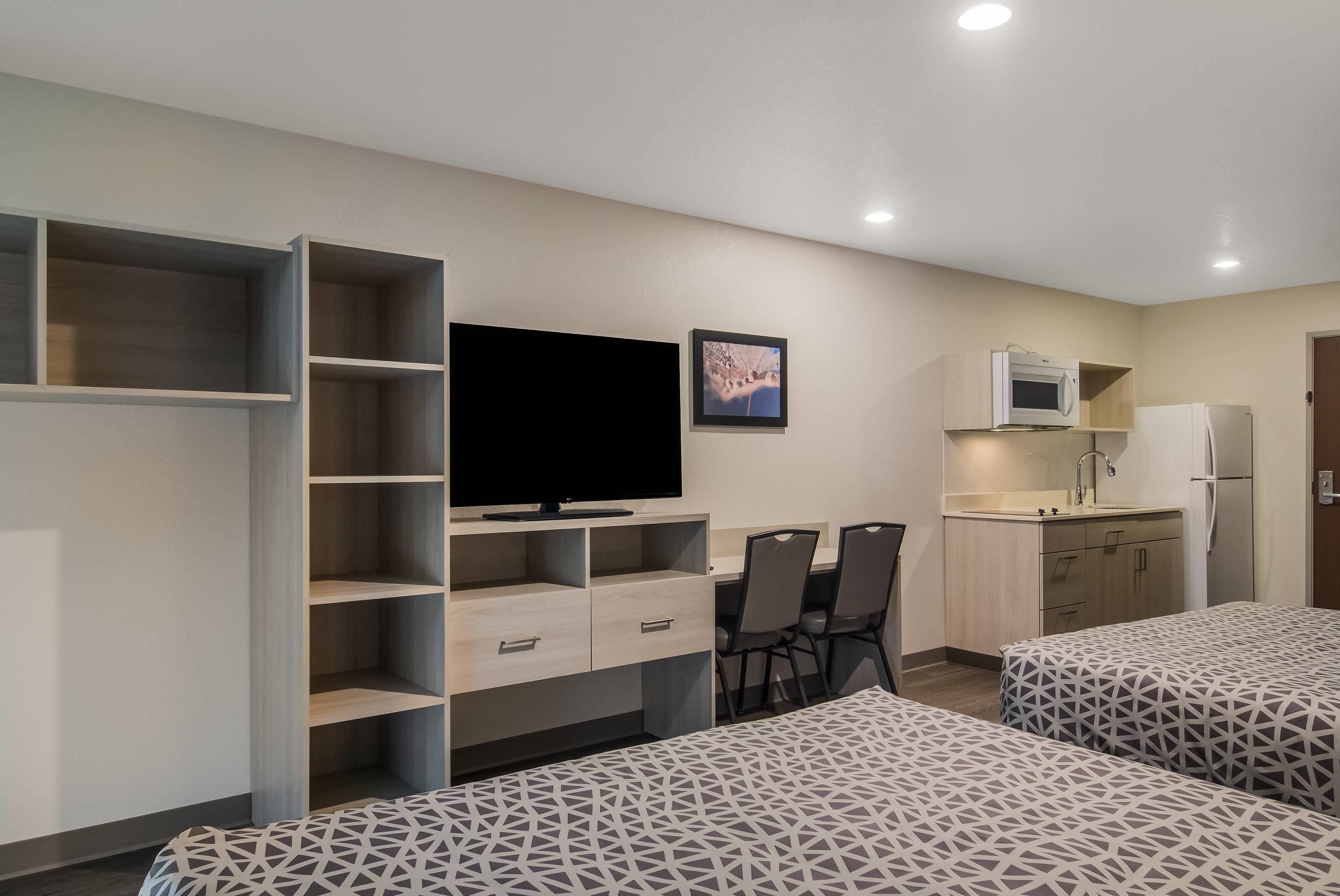 Een hotelkamer met een bed, een bureau met een flatscreen televisie, een kitchenette en een zithoek met stoelen.