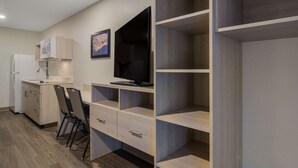 A compact living space with a kitchenette, a flat-screen TV mounted on the wall, and built-in shelving.