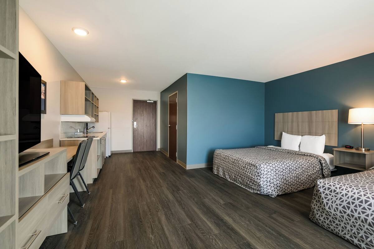 A modern hotel room with a desk, two beds, a TV, and a bathroom.