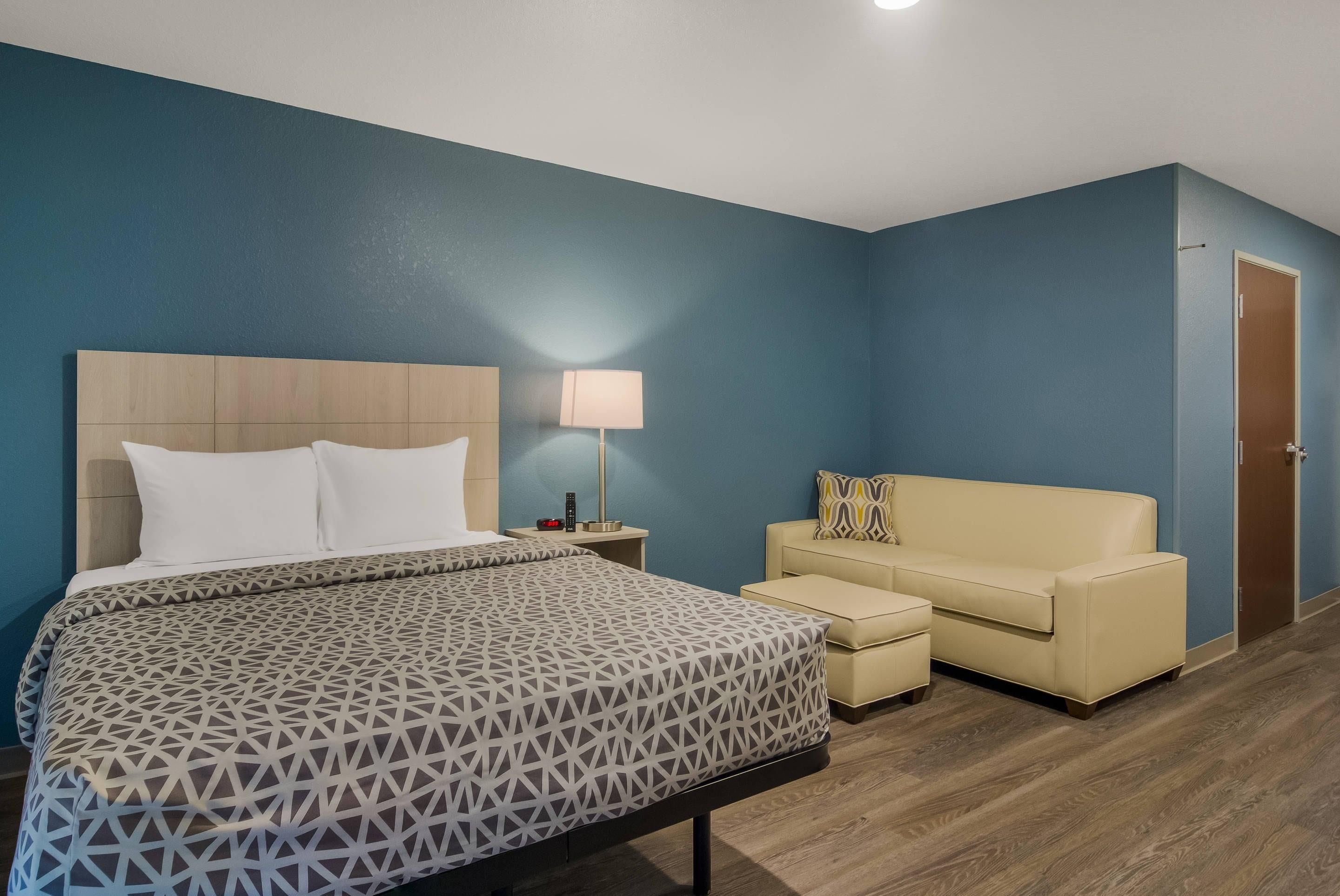 Una habitación de hotel con cama, mesita de noche con lámpara, sofá y puerta.