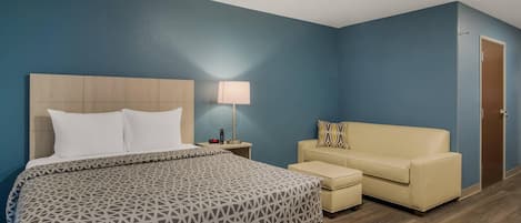 Una habitación de hotel con cama, mesita de noche con lámpara, sofá y puerta.