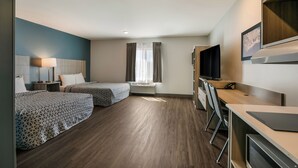 A hotel room with two beds, a desk, a chair, a TV, and a window with curtains.