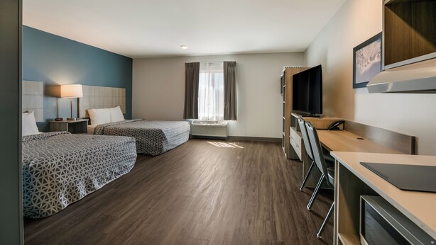 A hotel room with two beds, a desk, a chair, a TV, and a window with curtains. - Woodspring Suites Jacksonville Orange Park (Orange Park)