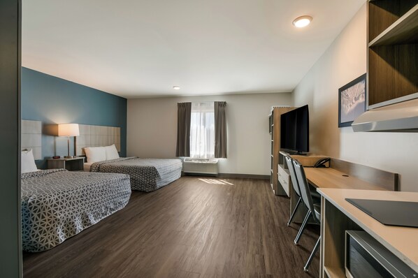 A hotel room with two beds, a desk, a chair, a TV, and a window with curtains. - Woodspring Suites Jacksonville Orange Park (Orange Park)