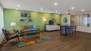 A modern living room with a green wall, a sofa, a coffee table, a dining table with chairs, and a cabinet.