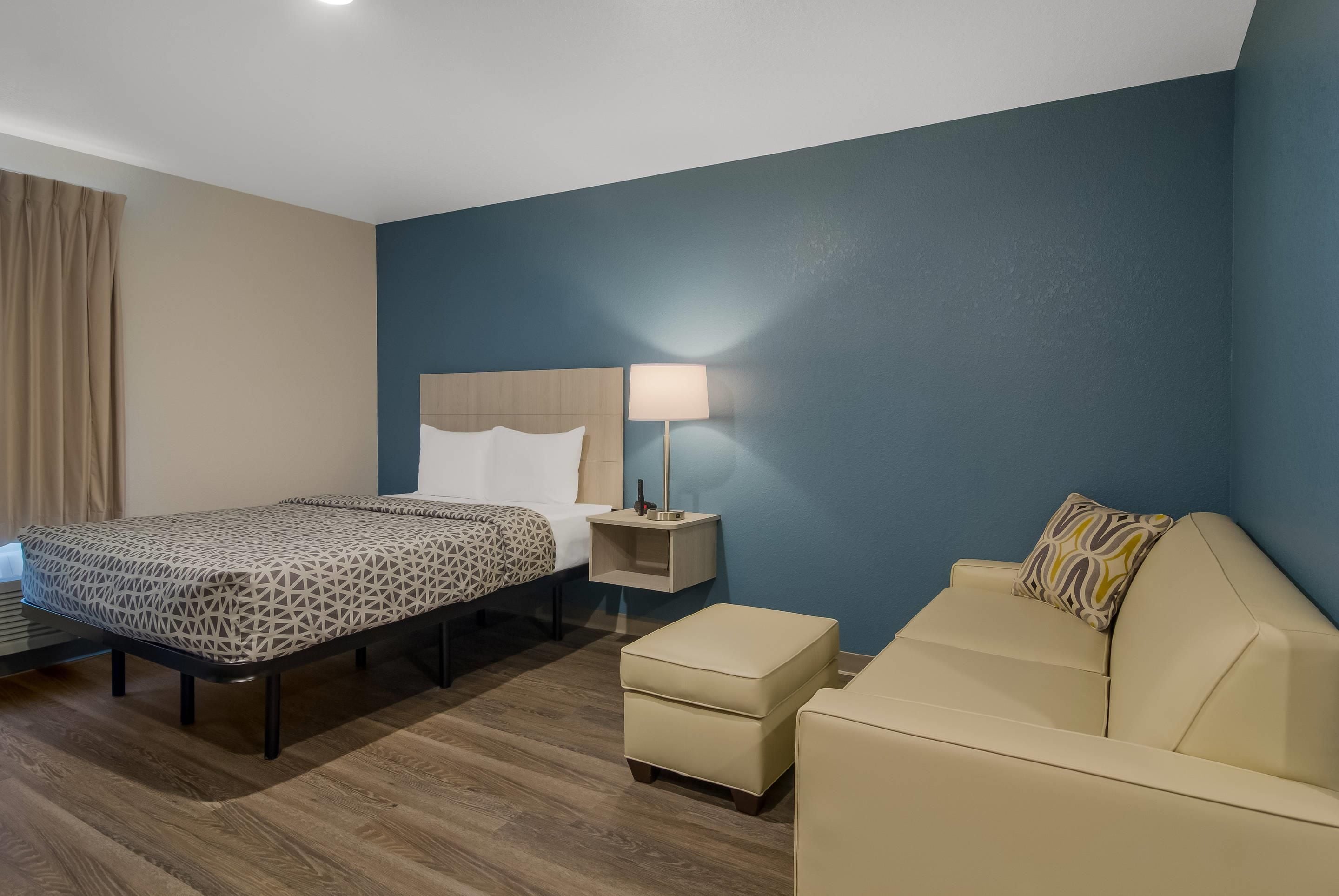 A hotel room with a bed, a bedside table with a lamp, a sofa, and a small table.