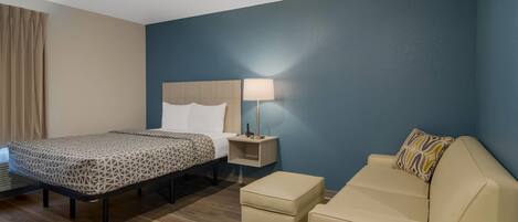 A hotel room with a bed, a bedside table with a lamp, a sofa, and a small table.