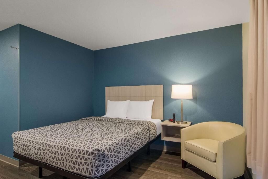 A hotel room with a bed, bedside table, lamp, and a chair.