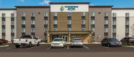 A multi-story hotel with a sign reading 'Woodspring Suites' and a parking lot with several cars.