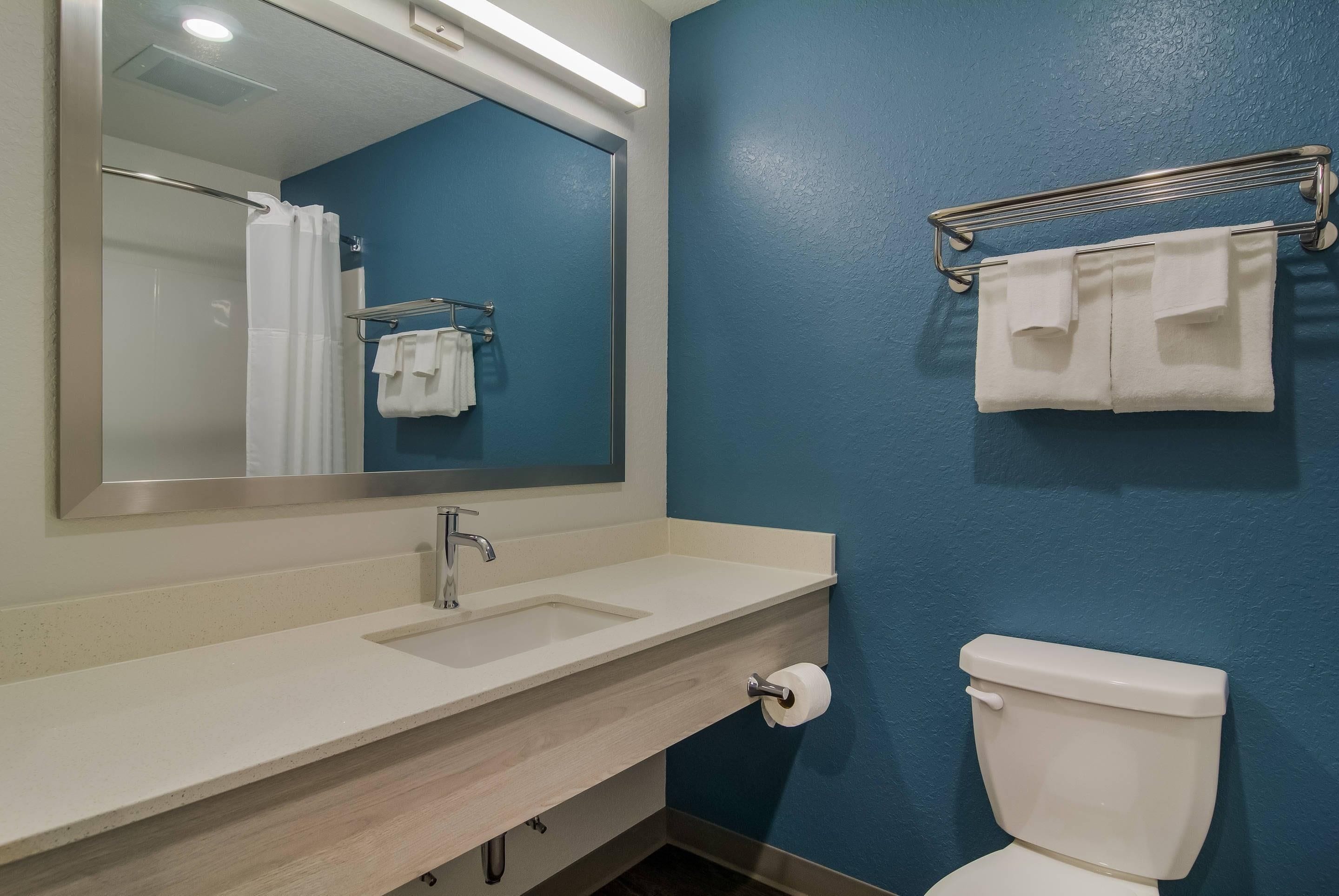 Un baño con lavamanos blanco, un espejo, un inodoro y un perchero para toallas.