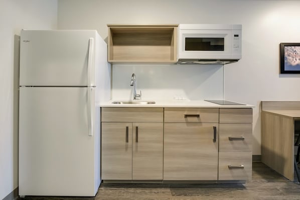 A compact kitchen with a white refrigerator, a microwave, and wooden cabinets. - Woodspring Suites Jacksonville Orange Park (Orange Park)