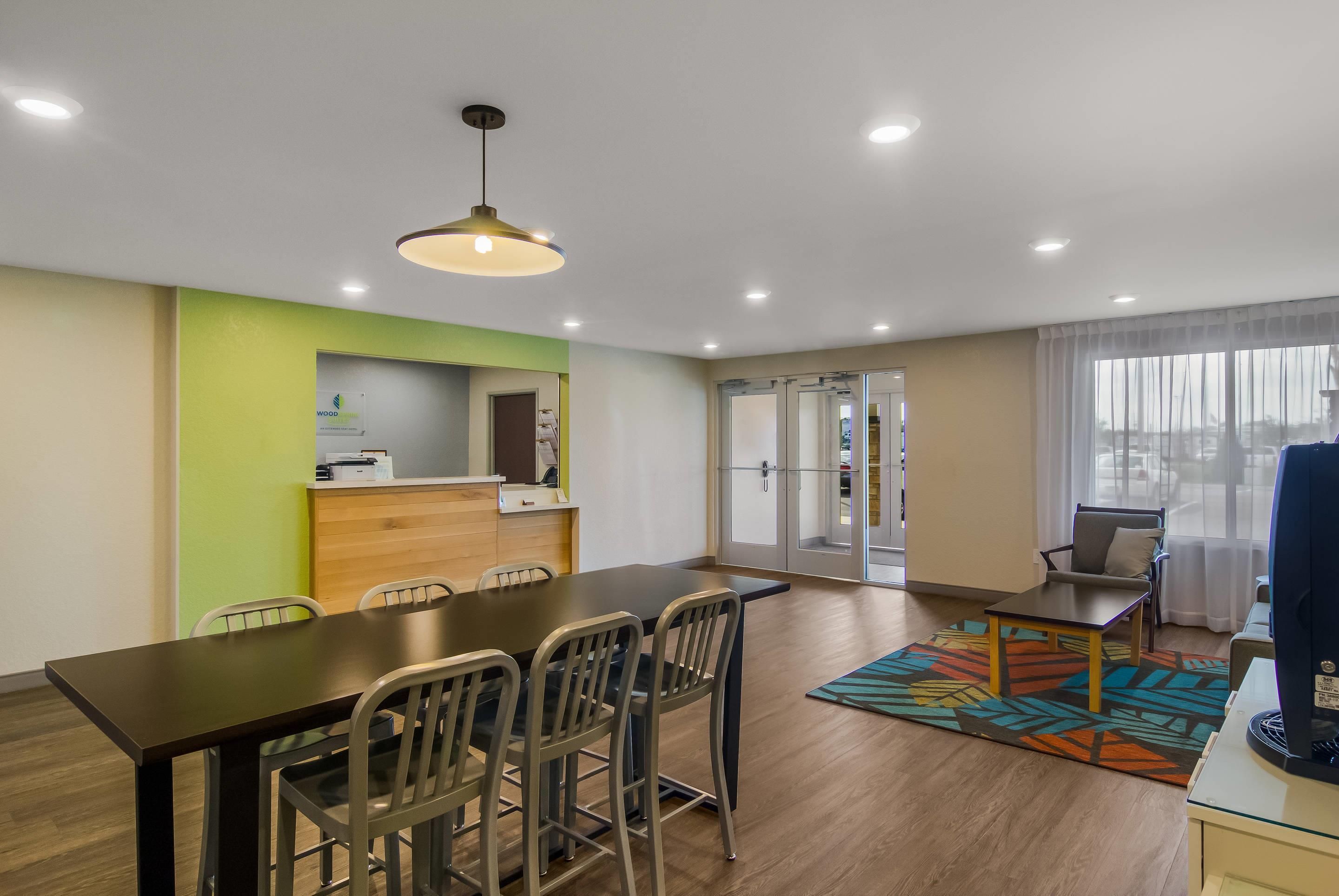 Habitación de hotel moderna con zona de comedor, mostrador de recepción y un amplio ventanal con cortinas.