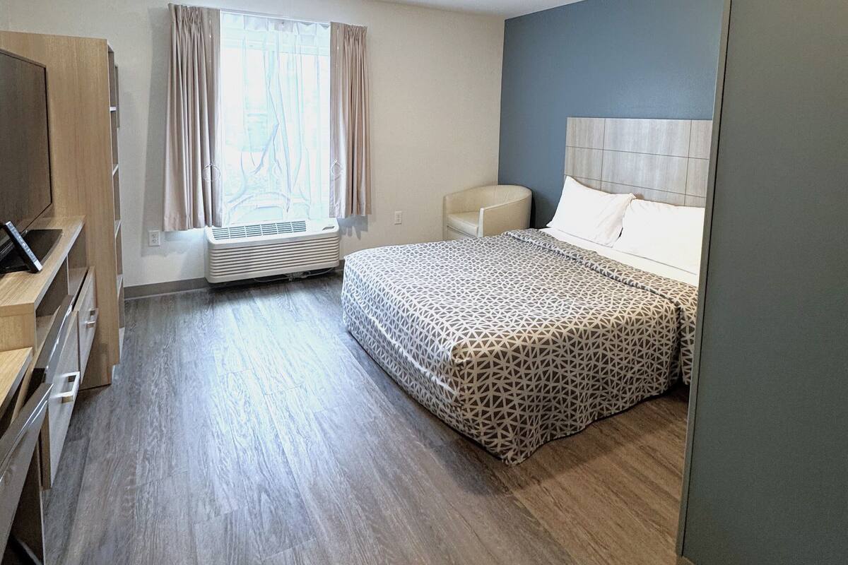 A hotel room with a bed, a desk, a chair, and a window with curtains.
