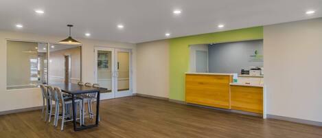 A modern hotel room with a dining area, a reception desk, and a large window.