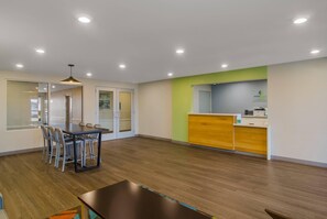 Una habitación de hotel moderna con zona de comedor, mostrador de recepción y un ventanal grande.