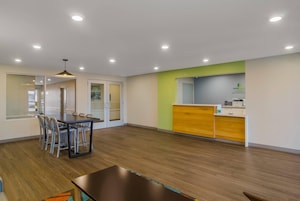 Una habitación de hotel moderna con zona de comedor, mostrador de recepción y un ventanal grande.