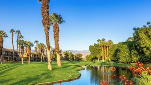A golf course with a pond, palm trees, and a mountain in the background.