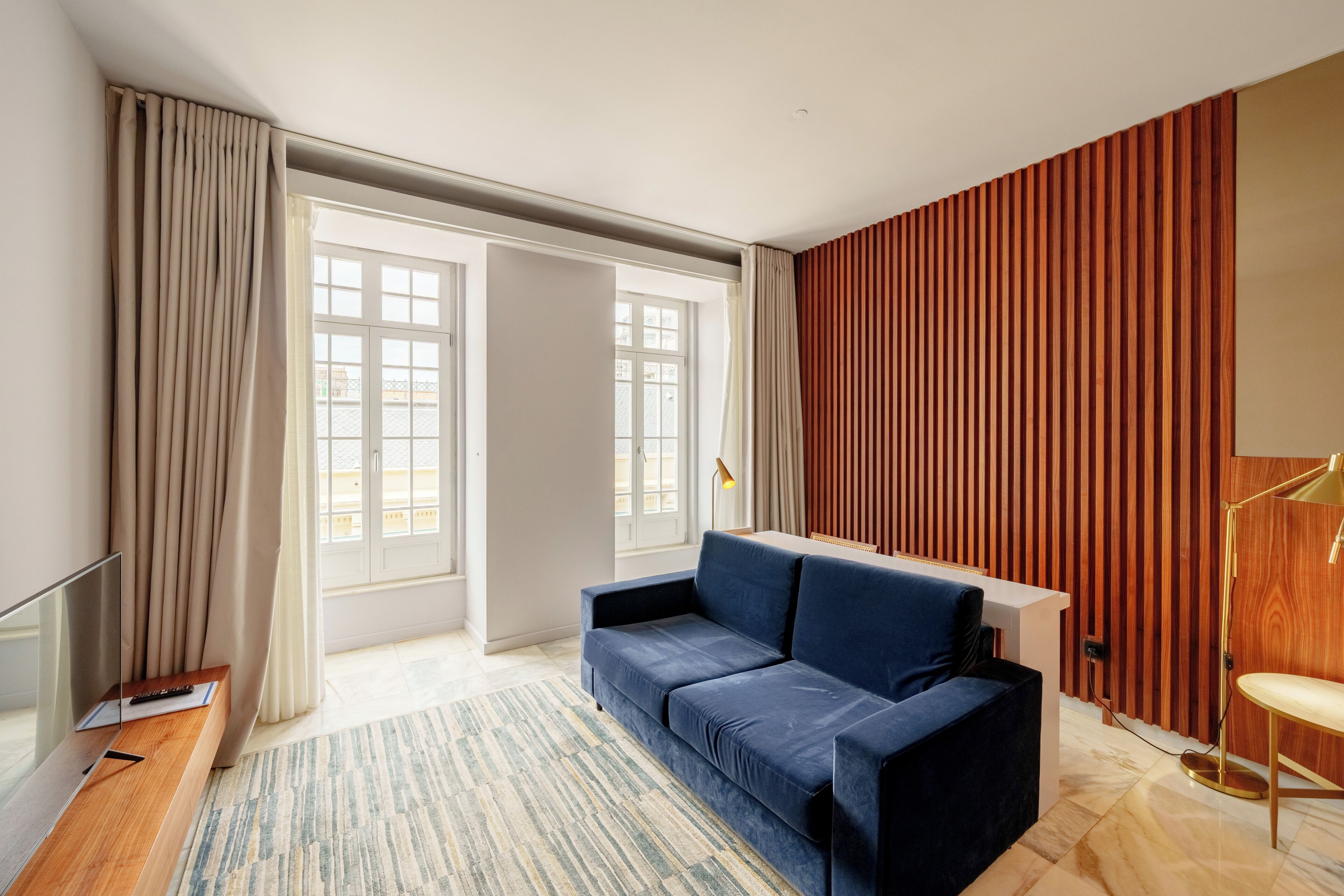 A modern living room with a sofa, a TV, and a wooden accent wall.