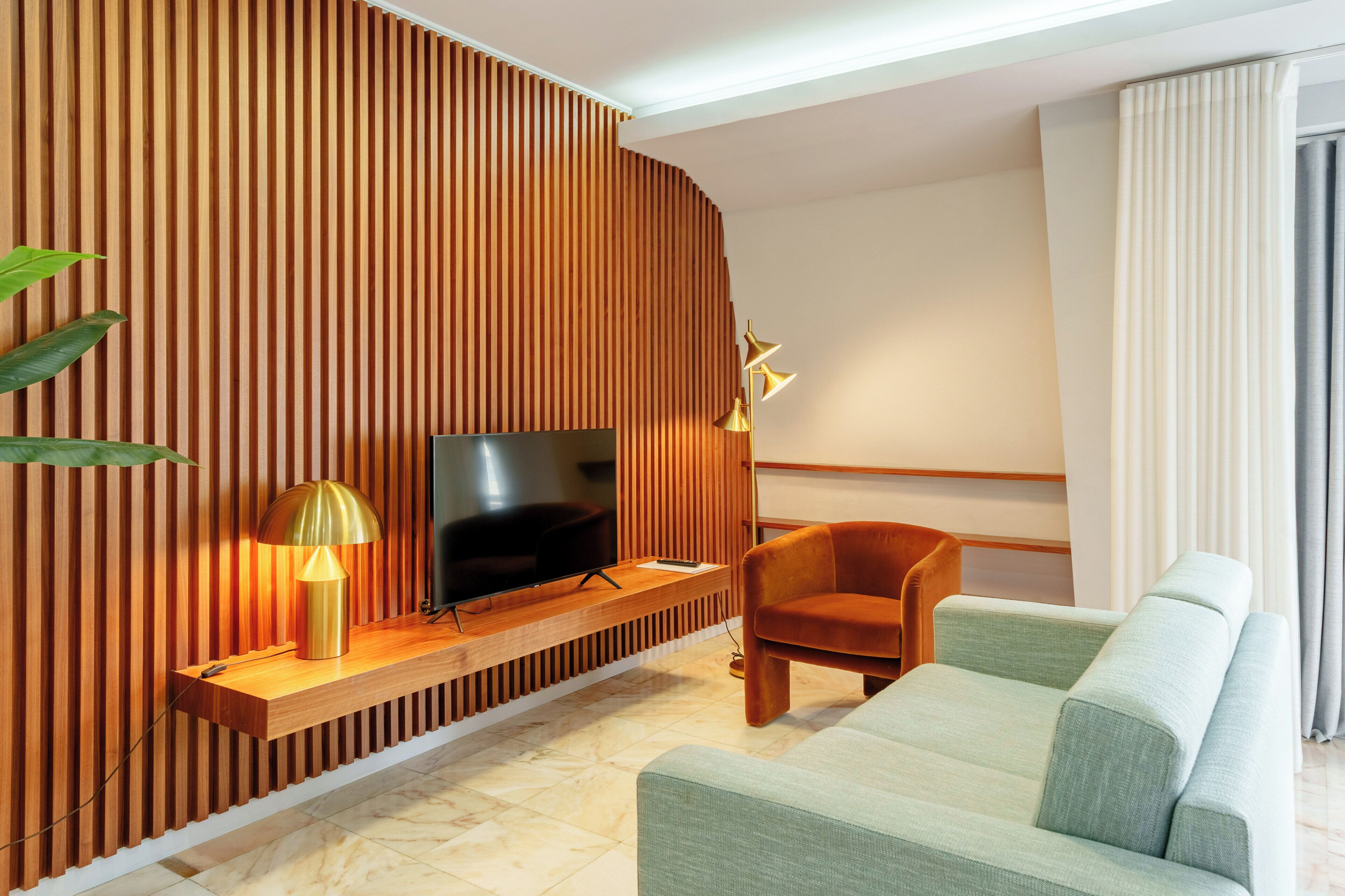 A modern living room with a TV, wooden slat wall, a sofa, a chair, and a lamp.
