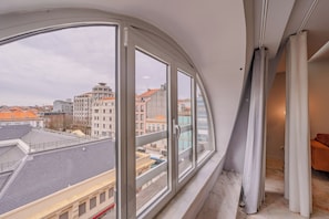 Ein Zimmer mit einem großen Bogenfenster, Blick auf eine Stadtlandschaft, einem Marmorboden und einem braunen Sofa.