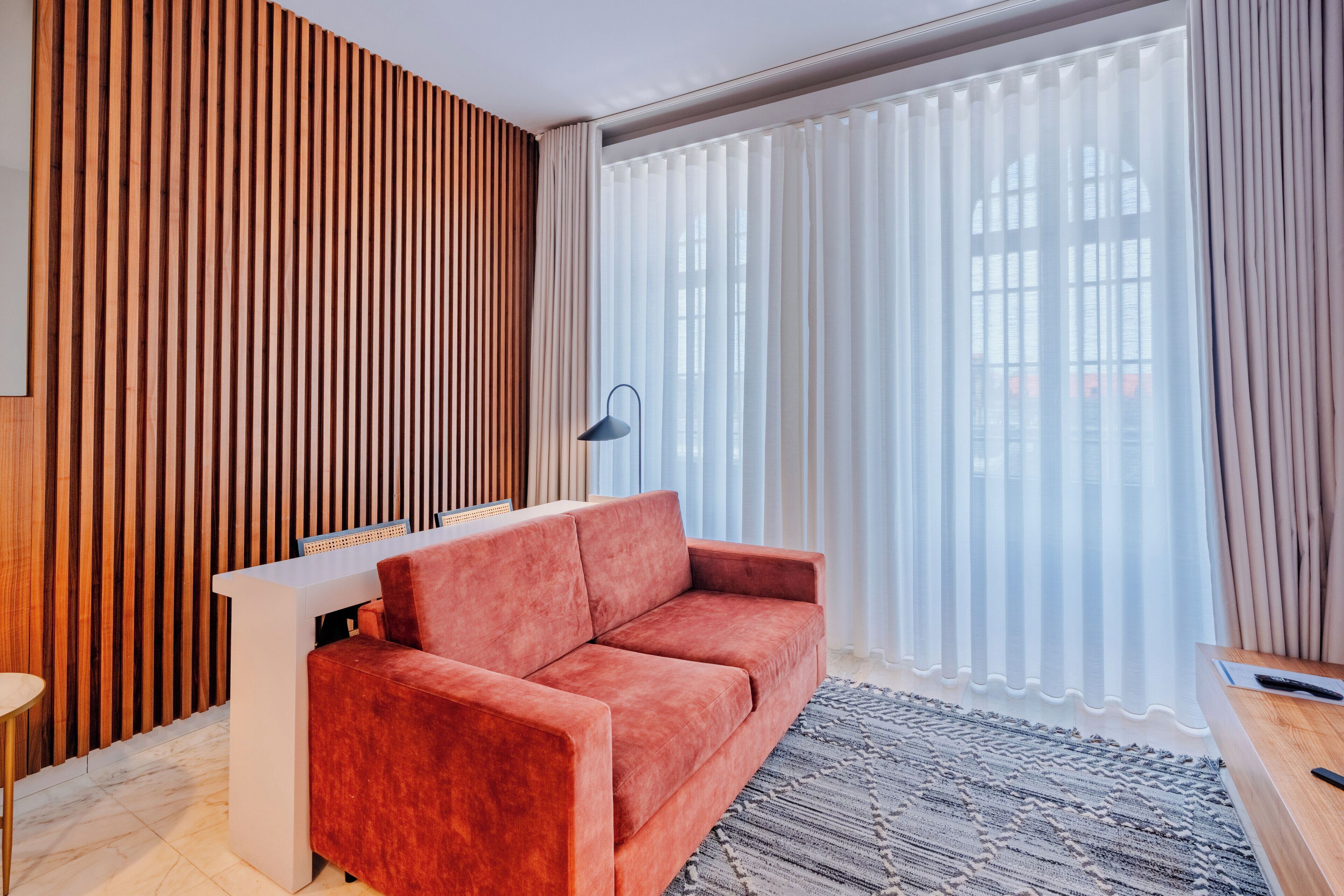 A modern living room with a red sofa, a white side table, and a patterned rug.
