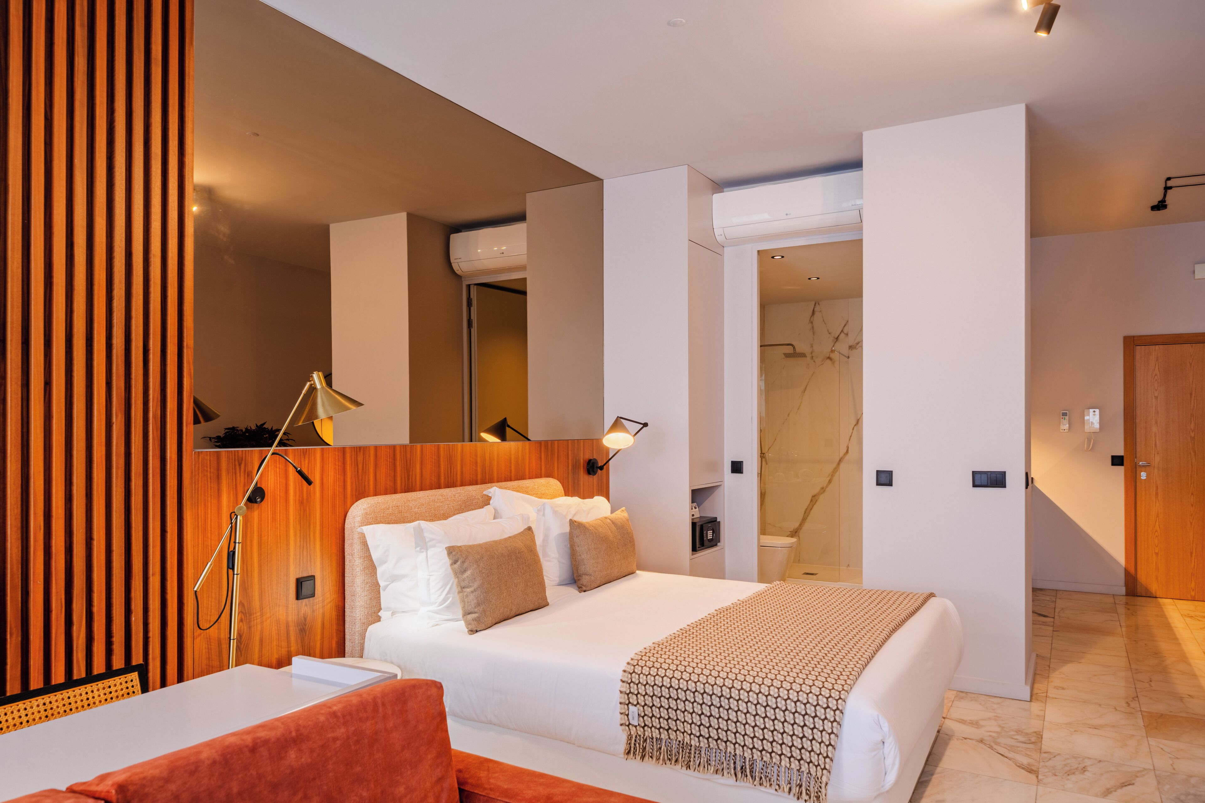 A modern hotel room with a large bed, a wooden accent wall, a mirror, and a bathroom visible through an open door.
