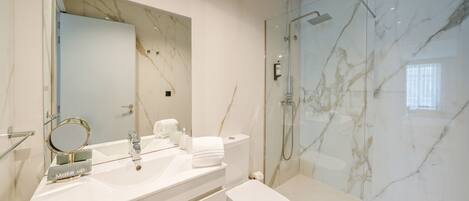 A modern bathroom with a marble wall, a glass-enclosed shower, a white sink with a mirror, and a toilet.