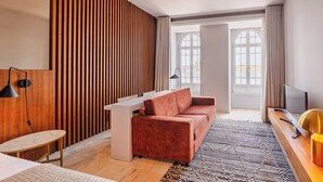 Ein modernes Wohnzimmer mit einer Couch, einem kleinen Tisch, einem Fernseher und einem großen Fenster mit Vorhängen.