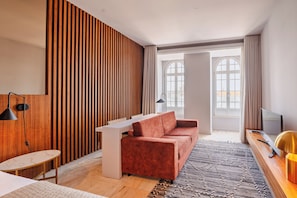 Un salon moderne avec un canapé, une petite table, un téléviseur et une grande fenêtre avec des rideaux.