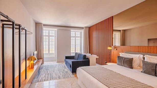 Ein modernes Hotelzimmer mit Bett, einer Couch, einem Schreibtisch und einem großen Fenster.
