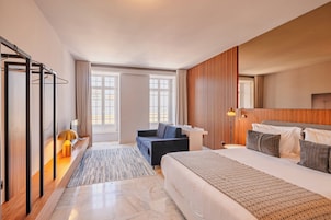 A modern hotel room with a bed, a sofa, a desk, and a large window.